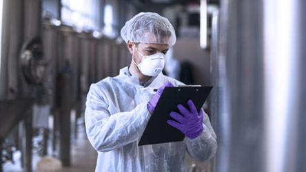 Laboratorijski radnik u zaštitnoj opremi pregleda epruvetu sa ljubičastom tečnošću u kontrolisanom okruženju.