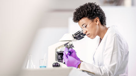 Naučnik u belom mantilu i zaštitnim rukavicama pažljivo analizira uzorak u laboratoriji.