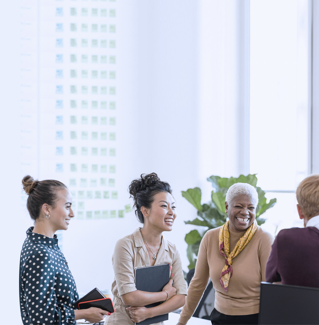 Grupa raznolikih kolega sedi za stolom u modernoj kancelariji, nasmejani i angažovani u razgovoru, simbolizujući inkluziju i timski rad.