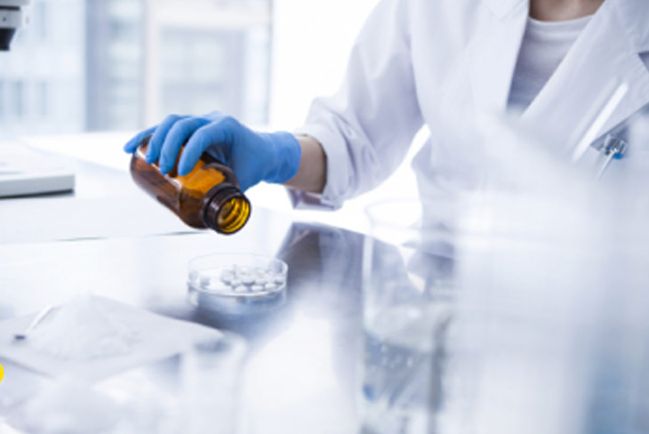 Naučnik u laboratorijskom mantilu i plavim rukavicama sipa bele tablete iz bočice u Petrijevu posudu.